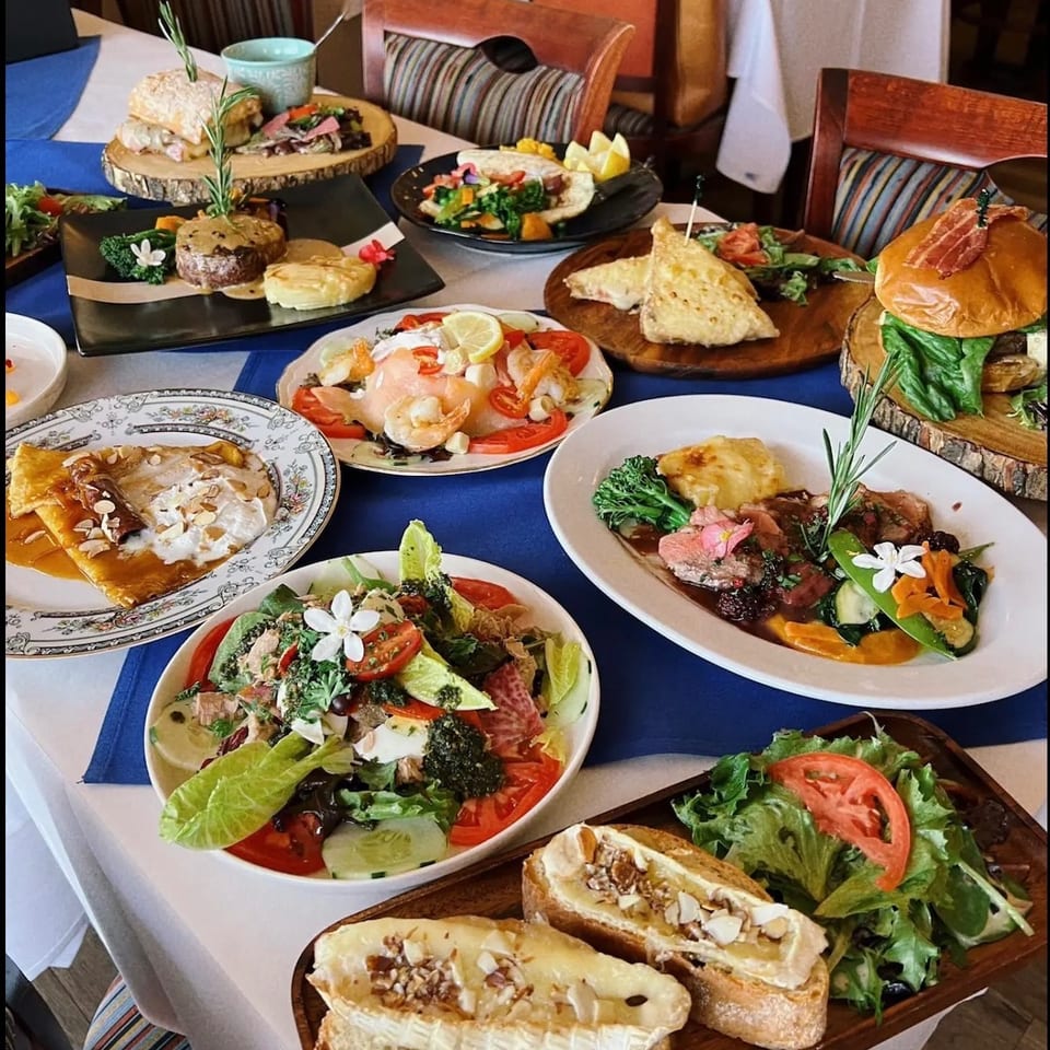 Restaurant table displaying assorted gourmet dishes, salads, sandwiches, grilled meats, seafood, and desserts in an elegant dining room.